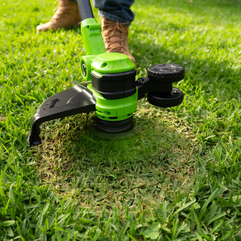 Green and black lawn trimmer being used on grass
