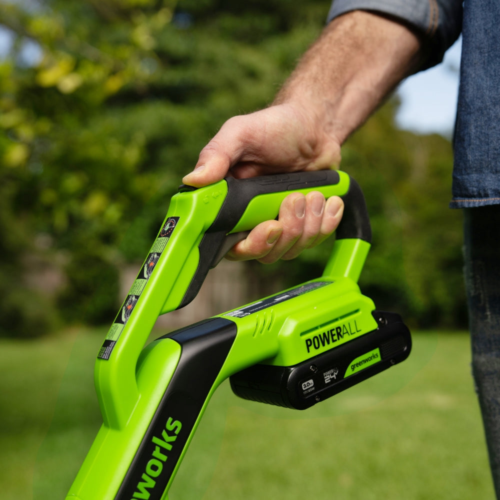 Person holding a green and black Powerworks tool with a blurred green outdoor background