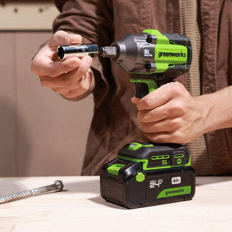 Person using a Greenworks cordless drill with a battery pack on a wooden surface.
